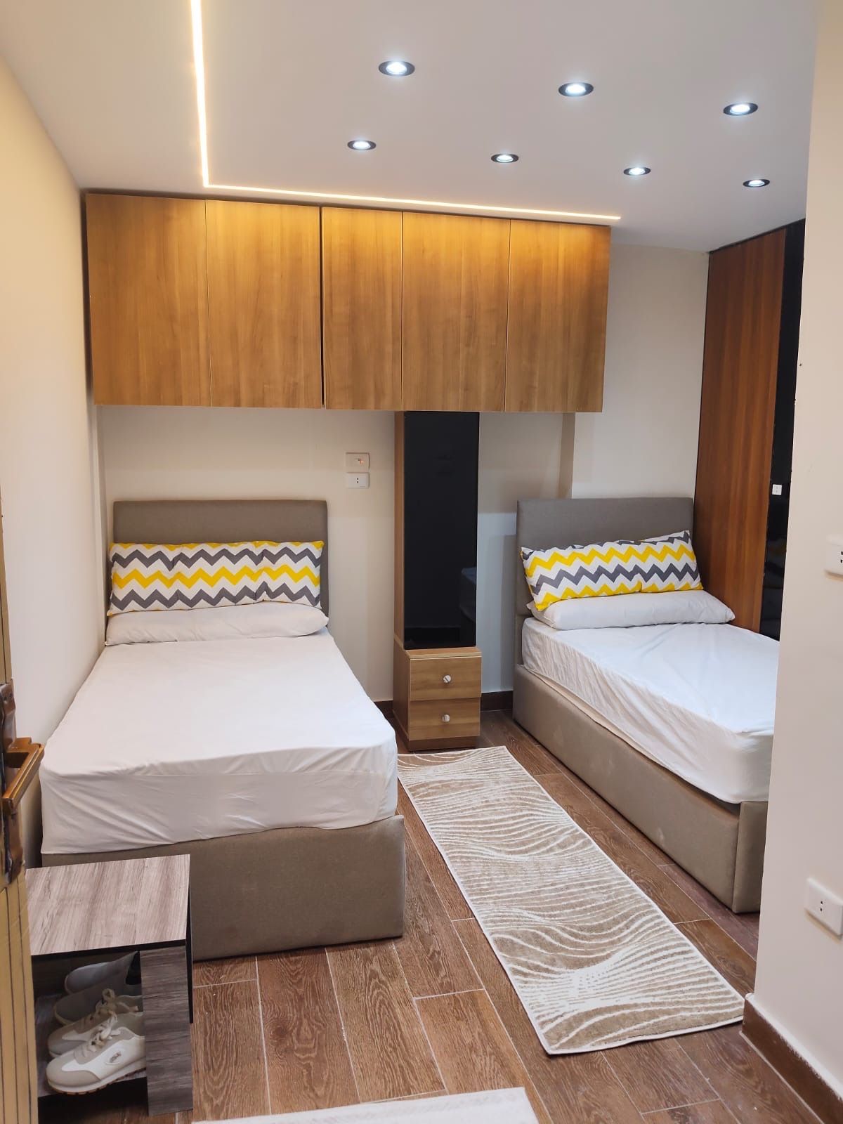A bedroom with two beds, wooden cabinets, a shoe cabinet, and a patterned rug.