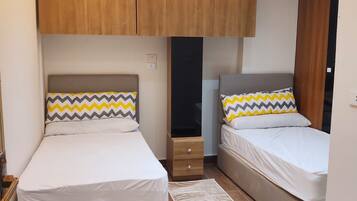 A bedroom with two beds, wooden cabinets, a shoe cabinet, and a patterned rug.