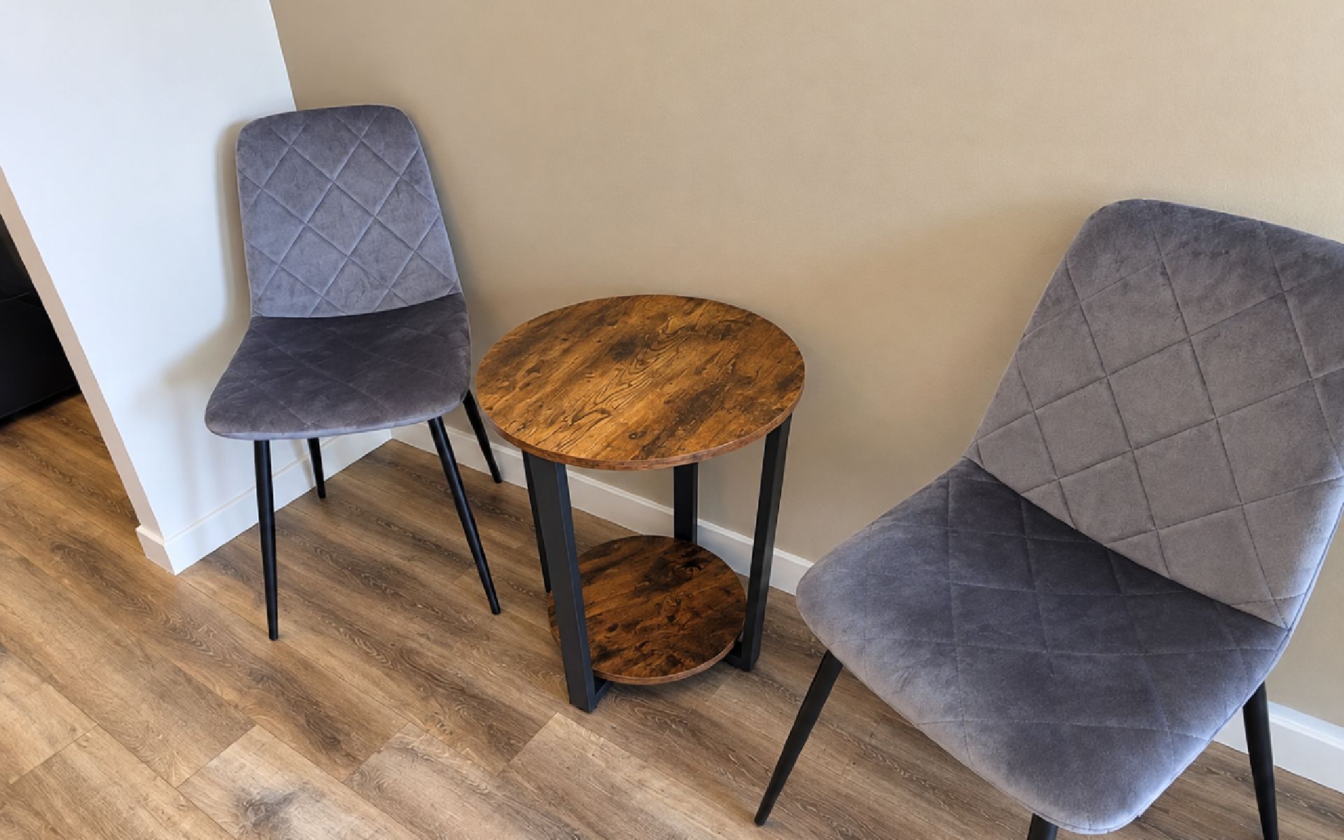 Zwei graue Polsterstühle mit schwarzen Beinen und ein runder Holztisch mit dunkler Holzoberfläche.