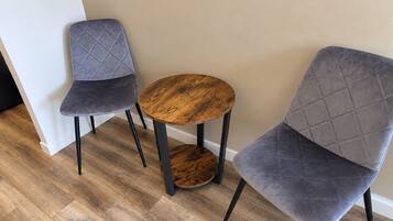 Zwei graue Polsterstühle mit schwarzen Beinen und ein runder Holztisch mit dunkler Holzoberfläche.