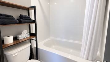 Ein Badezimmer mit einer weißen Badewanne, einer Toilette, einem Handtuchregal und einer Toilettenpapierrolle.