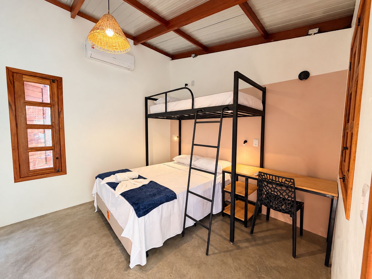 A bunk bed with a desk and chair, a hanging light fixture, and a window with blinds.