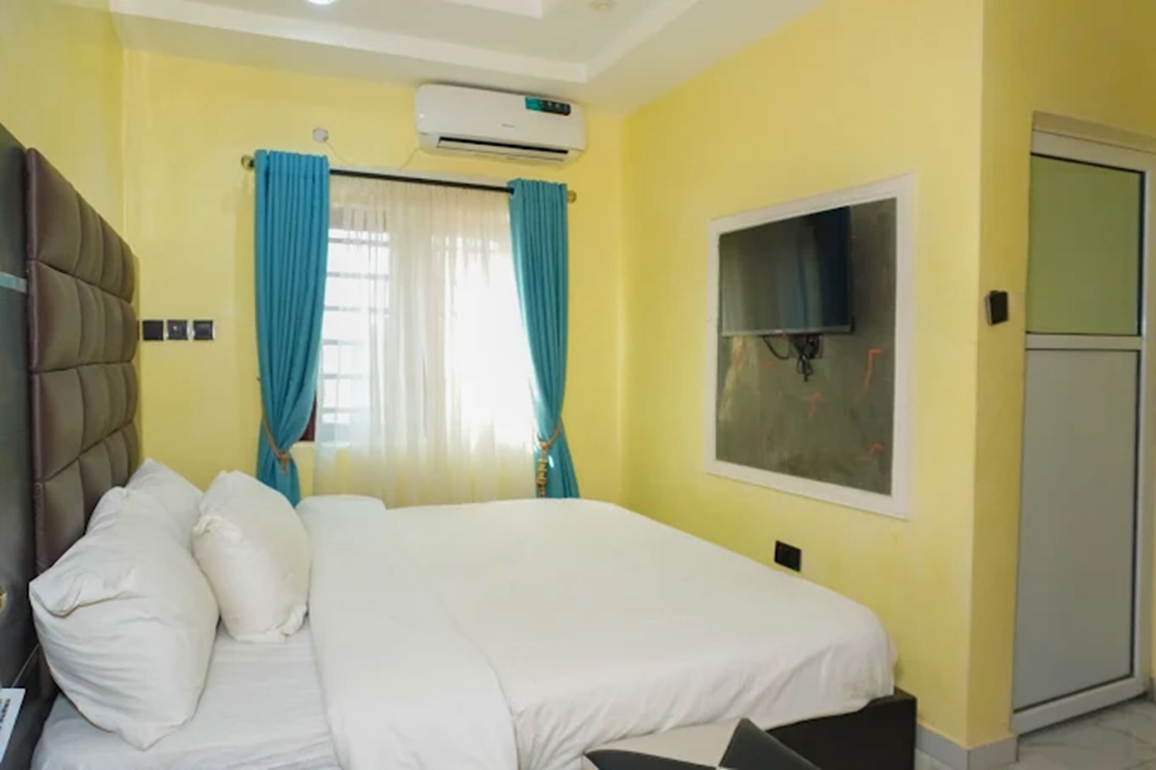 Una camera d'albergo con un letto, tende, un condizionatore d'aria e una finestra.