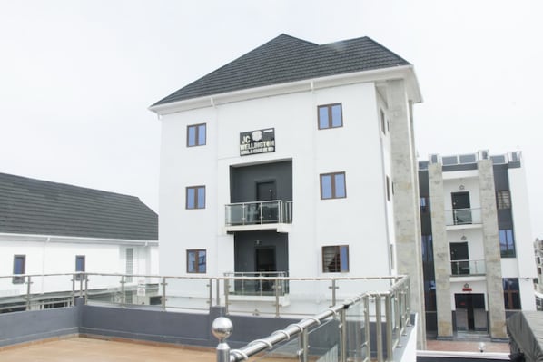 A multi-story building with a flat roof, a sign reading 'JC Wellington,' and a balcony with metal railings.