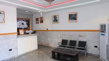 Zona de recepción con suelo de mármol, un mostrador de recepción, retratos enmarcados en la pared y una araña.