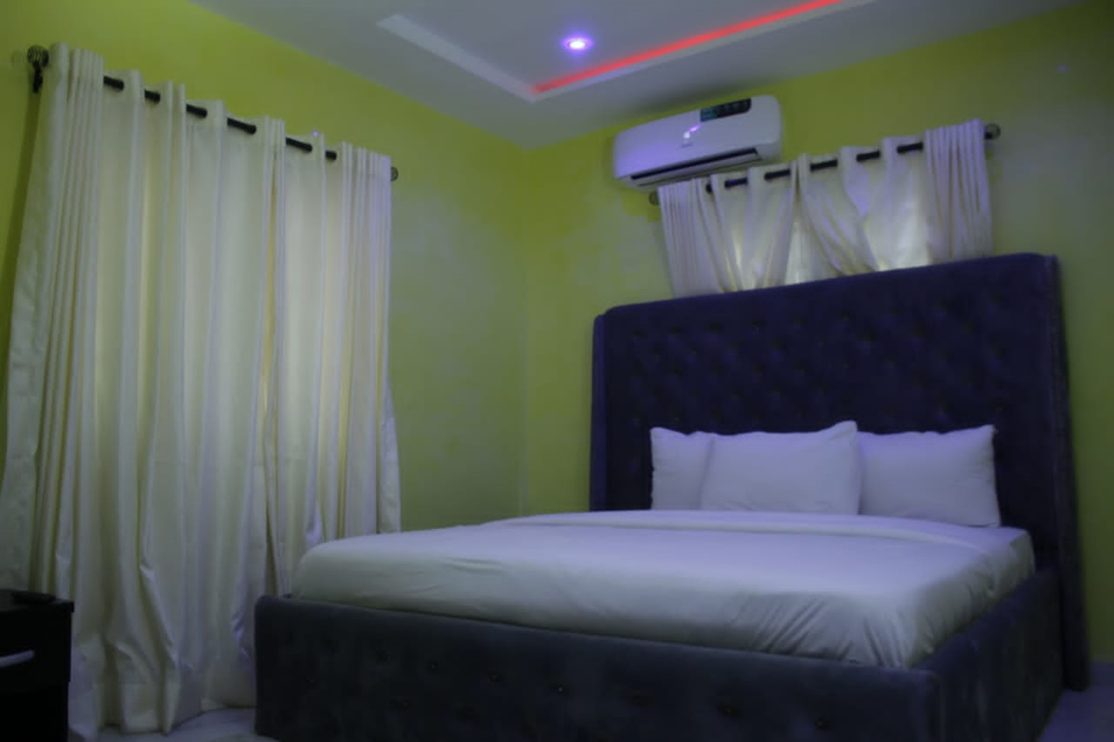 Una habitación con cama, cortinas, un equipo de aire acondicionado y una lámpara en el techo.