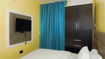 A hotel room with a bed, a television mounted on the wall, a wardrobe, and a curtain.