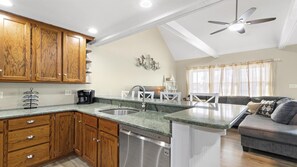 A kitchen with wooden cabinets, a dishwasher, a coffee maker, and a dining area with a sofa and curtains. - Large cape close to the beach & bay . Easy on & off the Island (Ship Bottom)