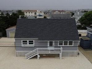 A two-story house with a grey exterior, a dark roof, and a small front porch with a white railing. - Large cape close to the beach & bay . Easy on & off the Island (Ship Bottom)
