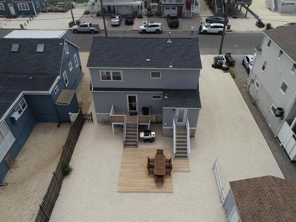 A two-story house with a patio area, a staircase leading to the upper floor, and a driveway with parked cars.
