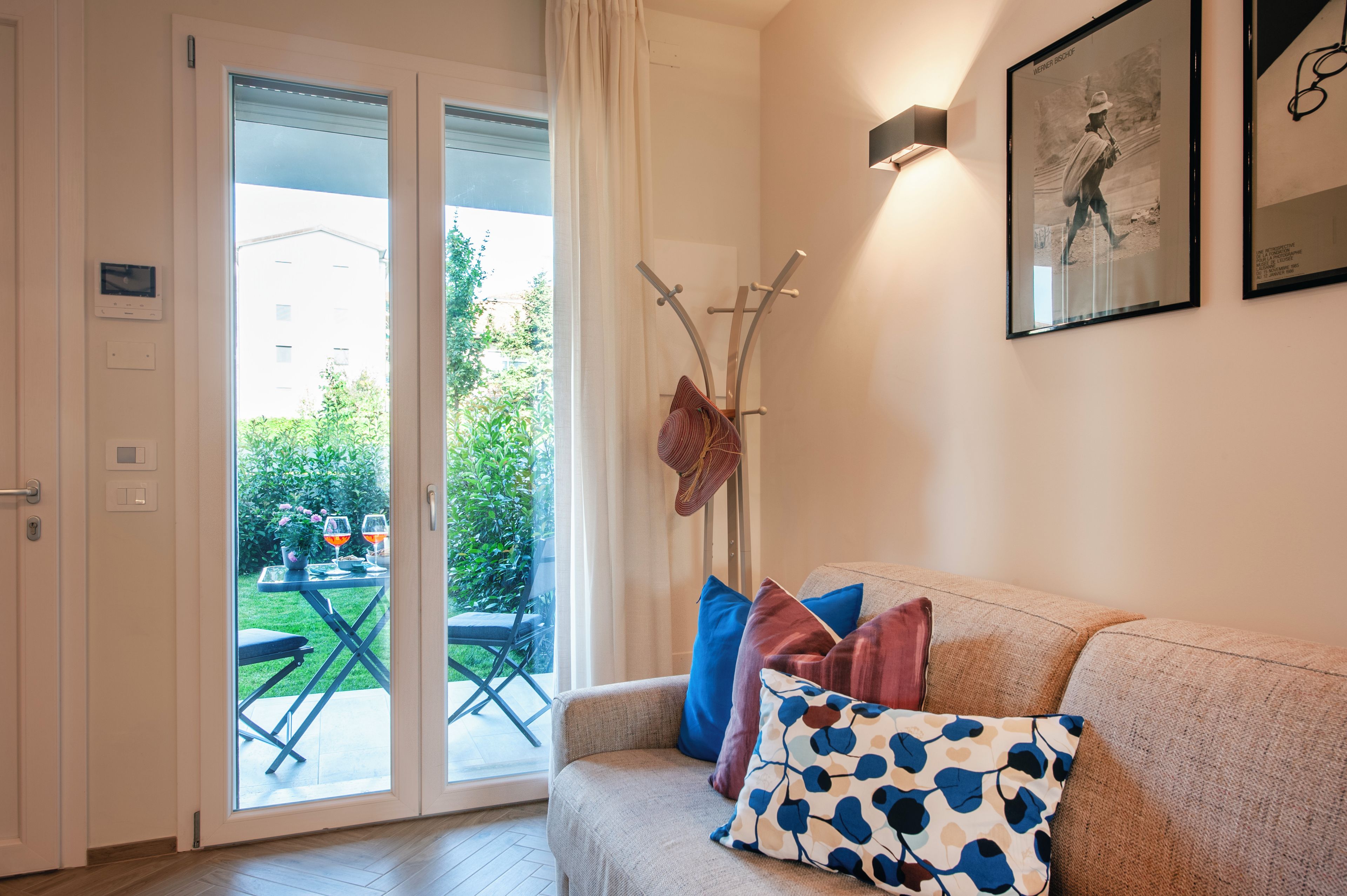 Een woonkamer met een bank, een kapstok en een deur die uitkomt op een balkon.