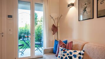 Een woonkamer met een bank, een kapstok en een deur die uitkomt op een balkon.