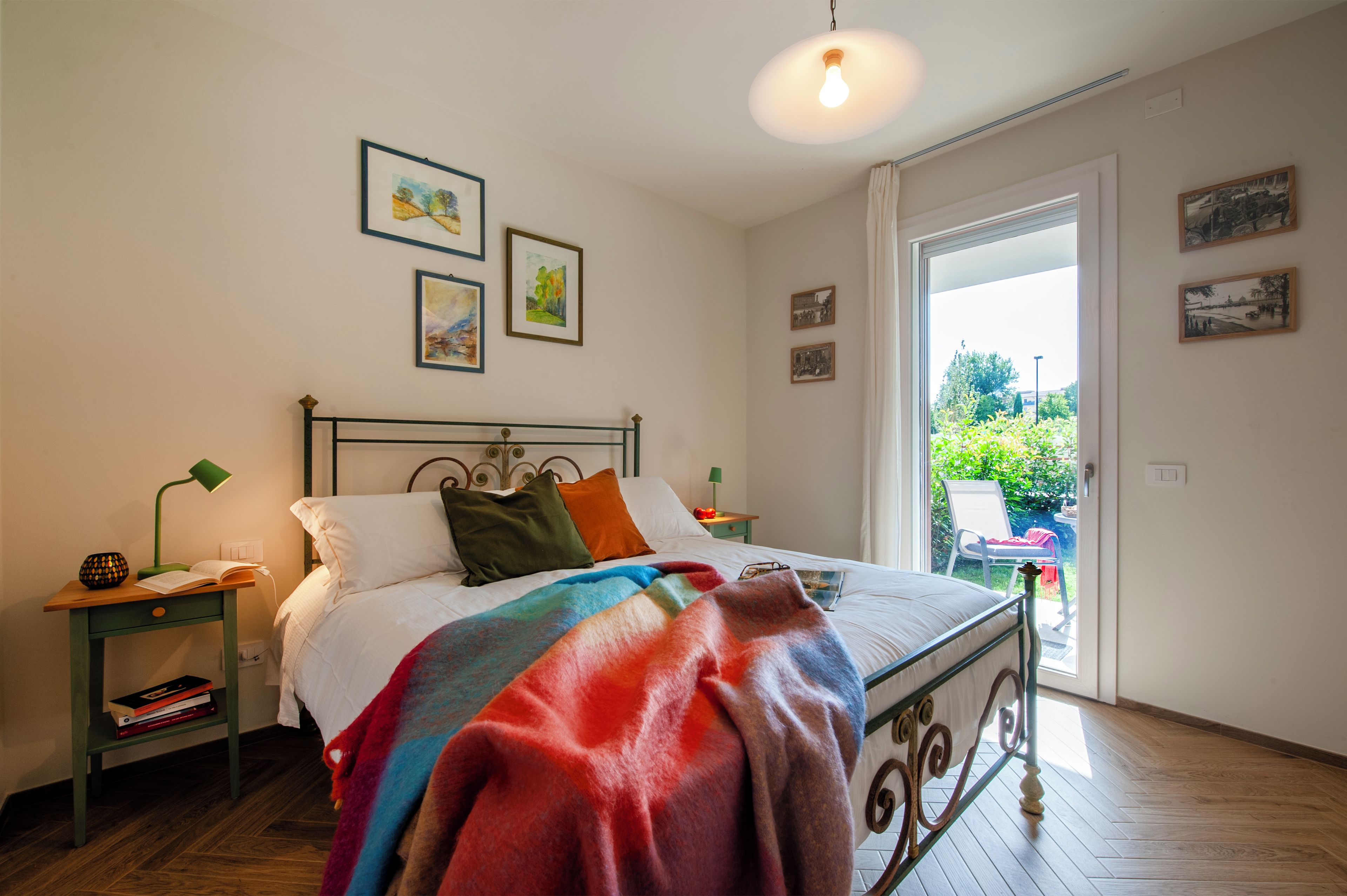 Een slaapkamer met een bed, nachtkastjes, een raam en kunstwerken aan de muren.