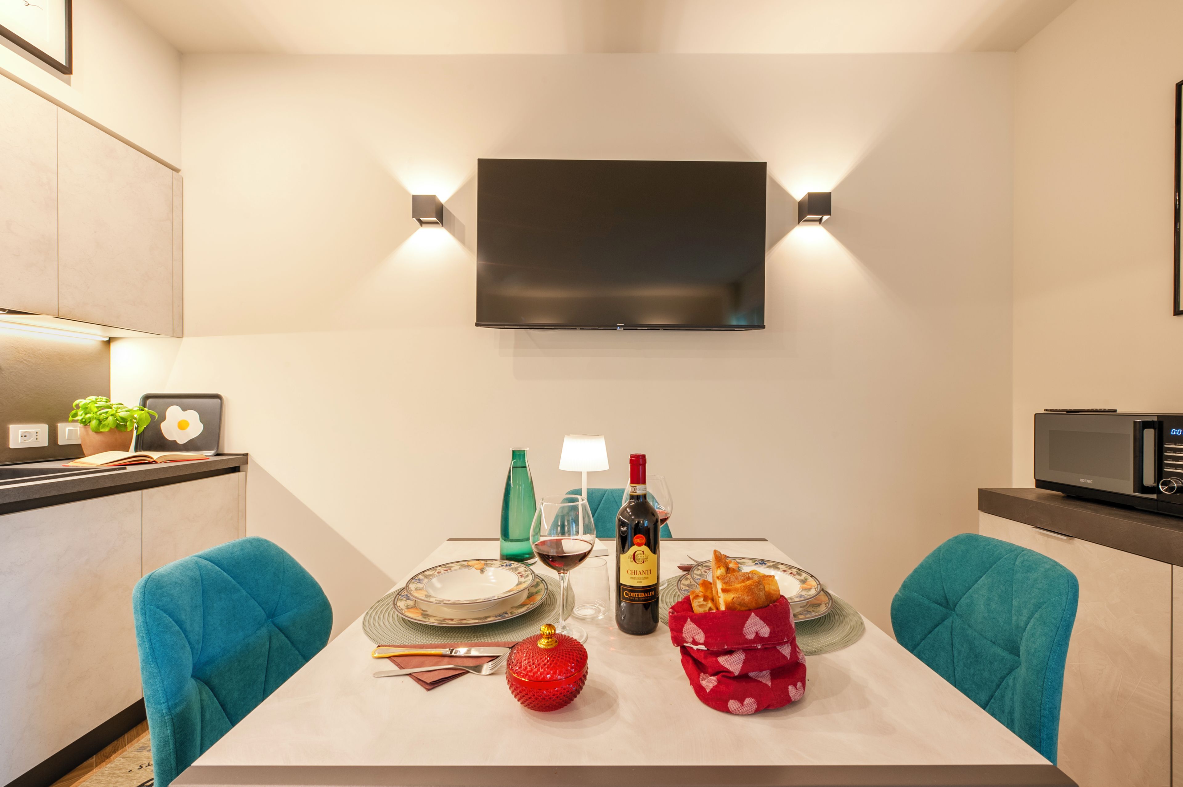 Een moderne eetruimte met een flatscreen televisie aan de muur, een gedekte tafel met borden, een wijnfles en een rode decoratie.