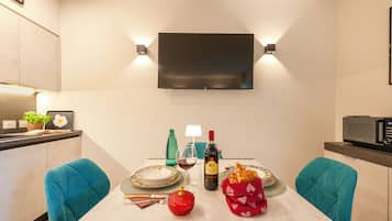 Een moderne eetruimte met een flatscreen televisie aan de muur, een gedekte tafel met borden, een wijnfles en een rode decoratie.