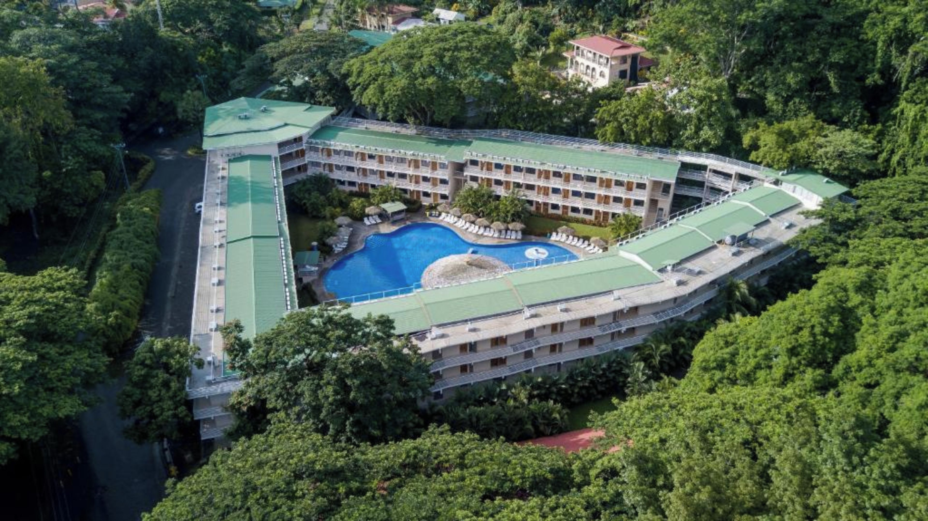 A resort with a central swimming pool, multiple balconies, and lush surrounding greenery.