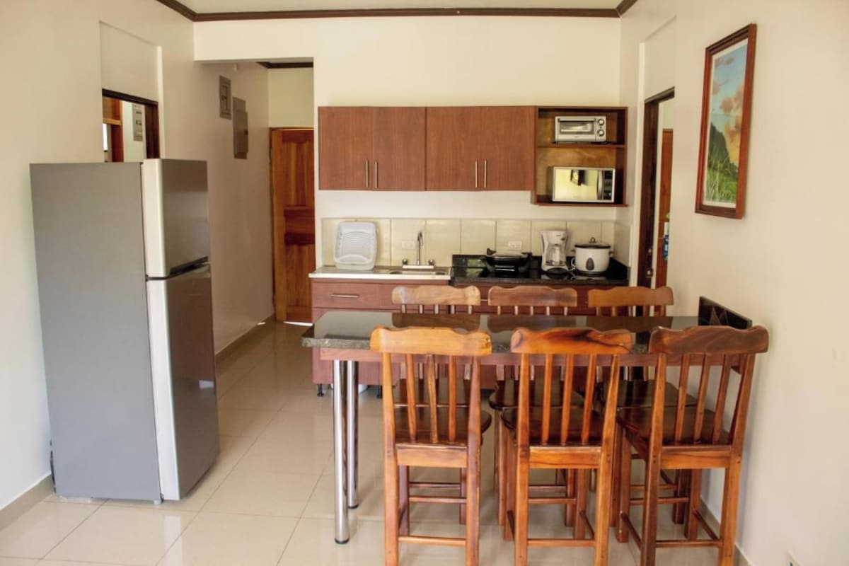 Una cocina con armarios de madera, un refrigerador, un microondas y una mesa de comedor con sillas.
