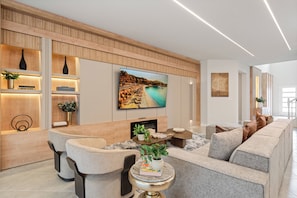 A modern living room with a flat-screen TV mounted on the wall, a fireplace, and a seating area with a sofa and chairs. - Brand New Disney-Themed 8BR Home | Windsor Cay (Clermont)