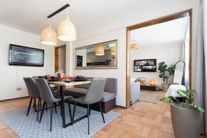Espaço de refeições moderno com mesa de madeira, cadeiras estofadas em cinza e iluminação pendente.