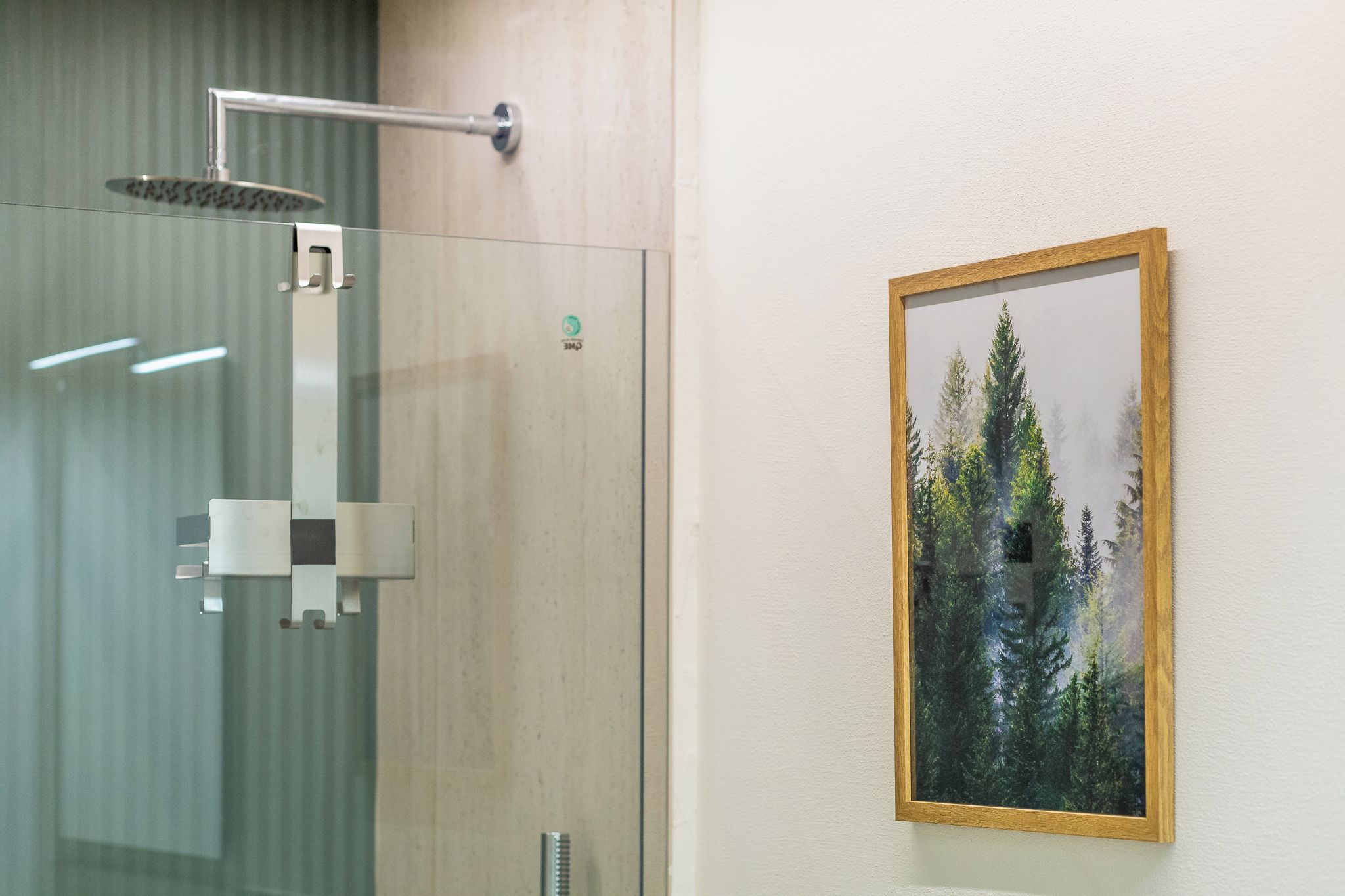 Une douche avec une paroi en verre et un tableau encadré représentant des arbres accroché au mur.