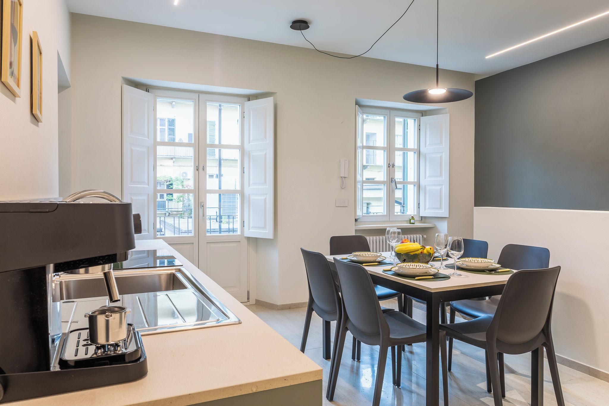 A modern kitchen with a built-in espresso machine, a dining area with a table set for four, and large windows providing natural light.