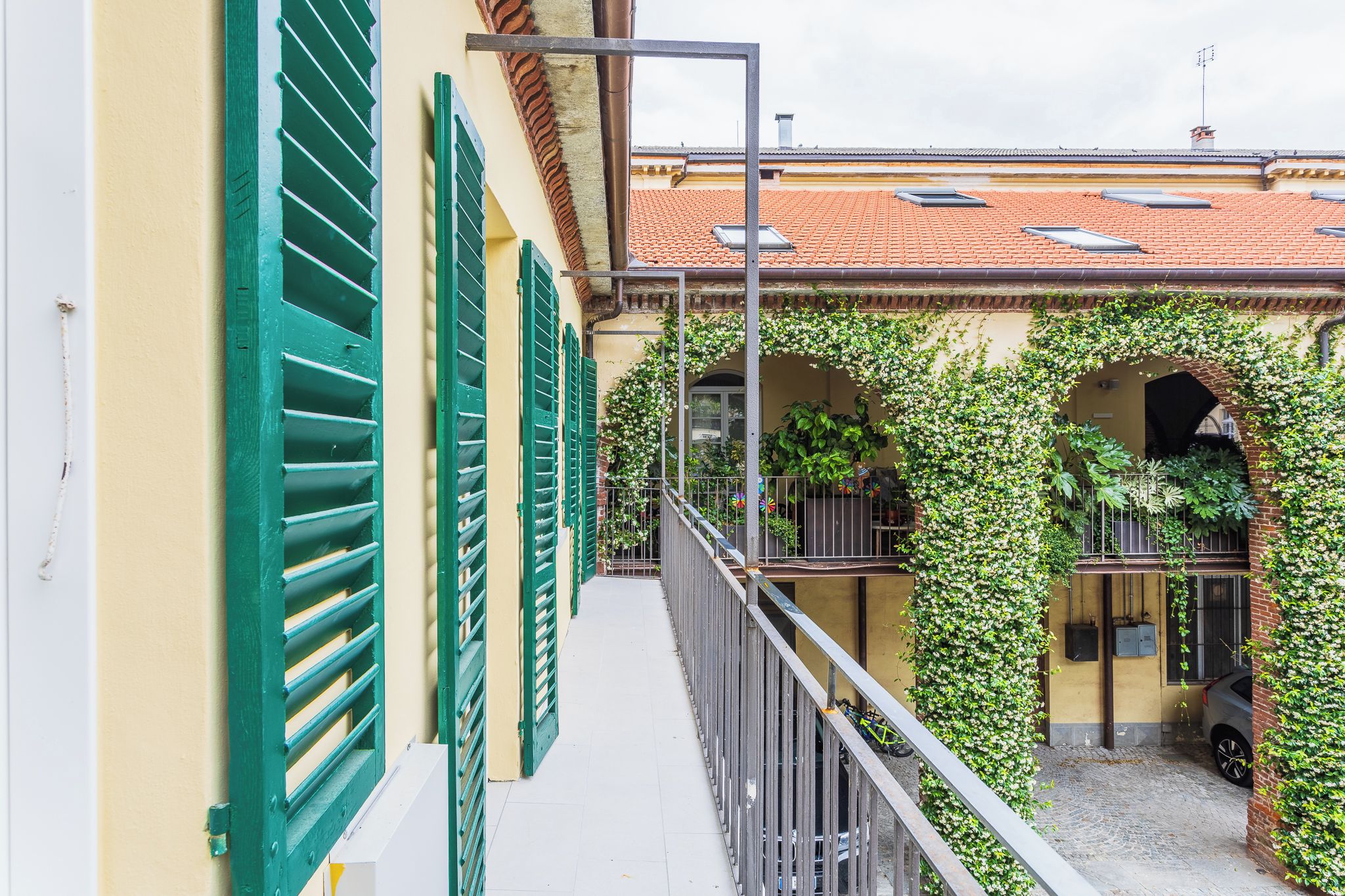 Un corridoio stretto con un balcone, persiane verdi e un tetto in tegole.