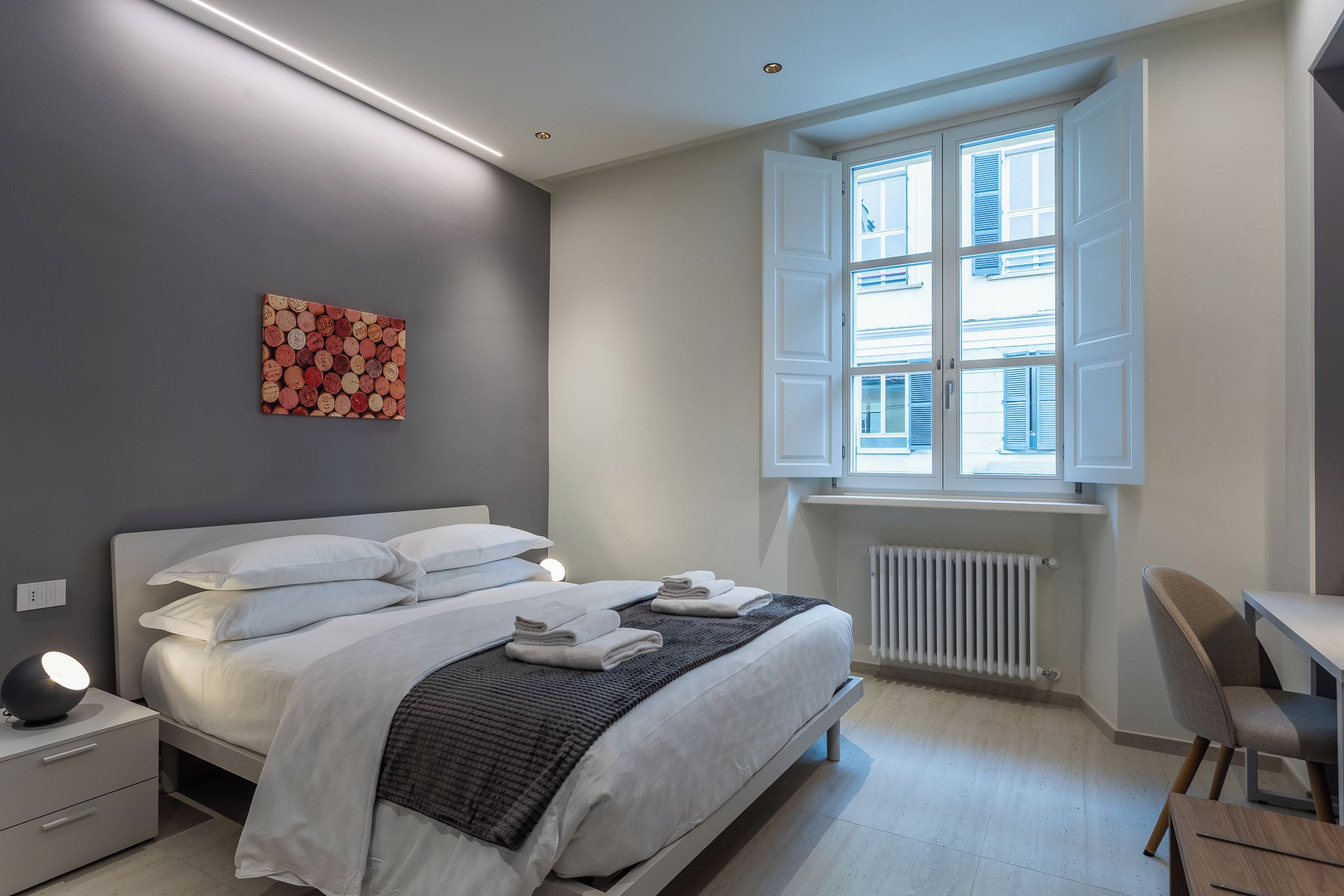 A modern bedroom with a bed, bedside table, lamp, and a window with blinds.