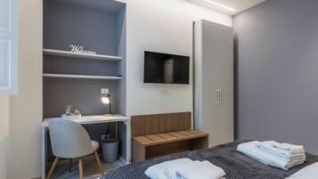 Une chambre d’hôtel moderne équipée d’un bureau, d’une chaise, d’une télévision, d’une armoire et de serviettes soigneusement pliées.