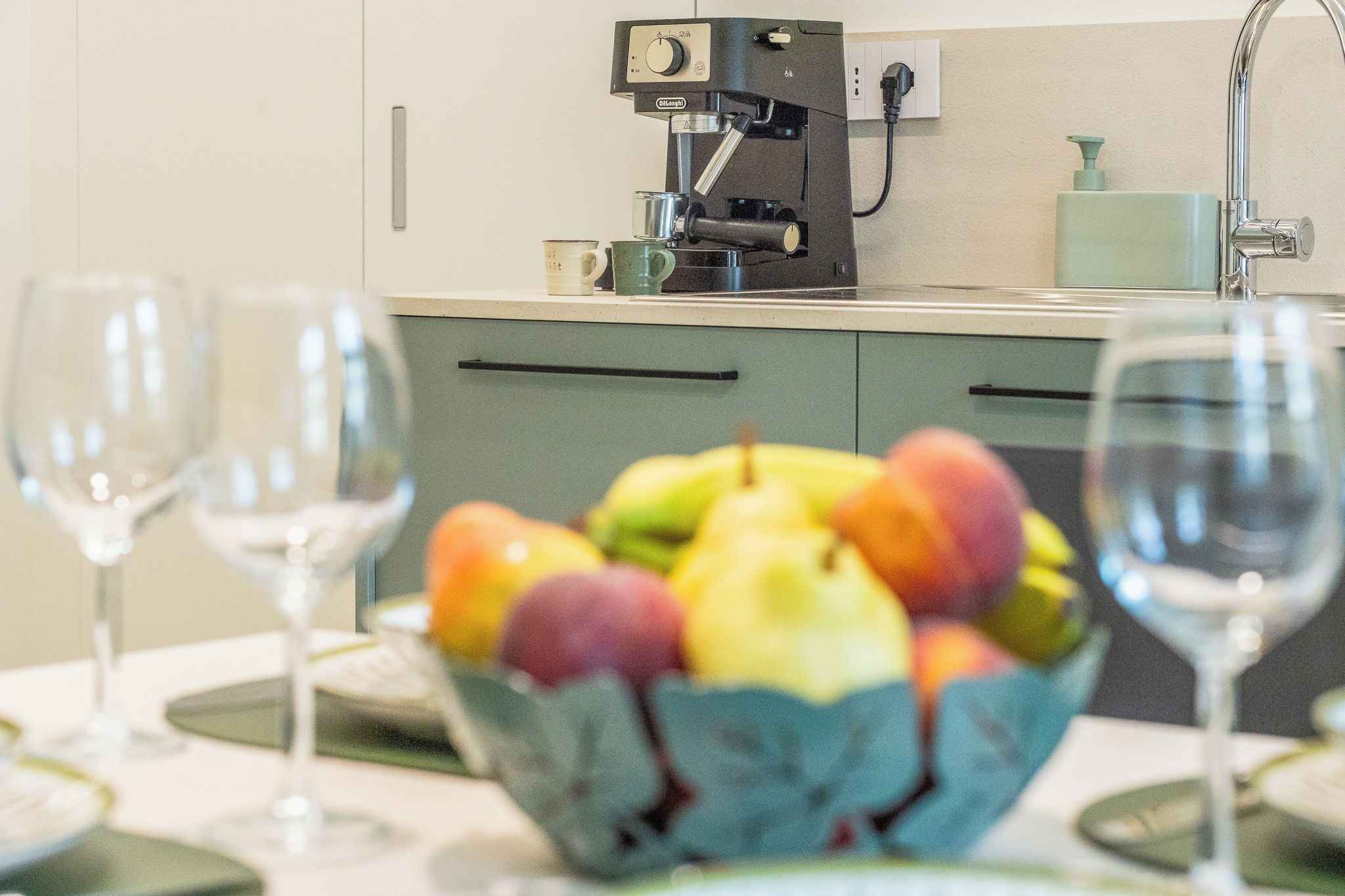 A kitchen with a coffee machine, a fruit bowl on the counter, and wine glasses.