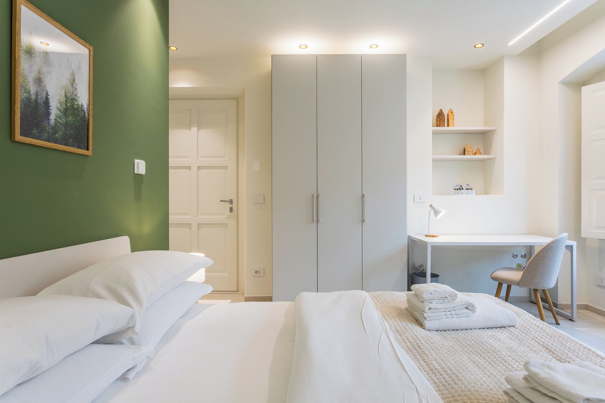 Una camera d'albergo con un letto, una scrivania, una sedia e un armadio.