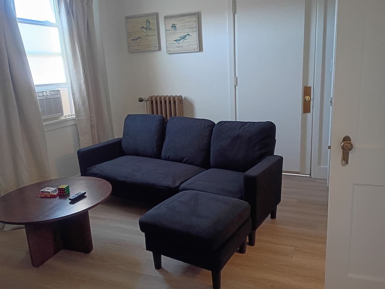A living room with a dark-colored sofa, a small round coffee table, and a radiator.