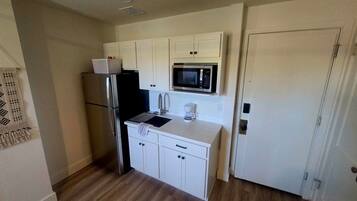 A compact kitchen with white cabinets, a stainless steel refrigerator, a microwave, and a coffee maker.