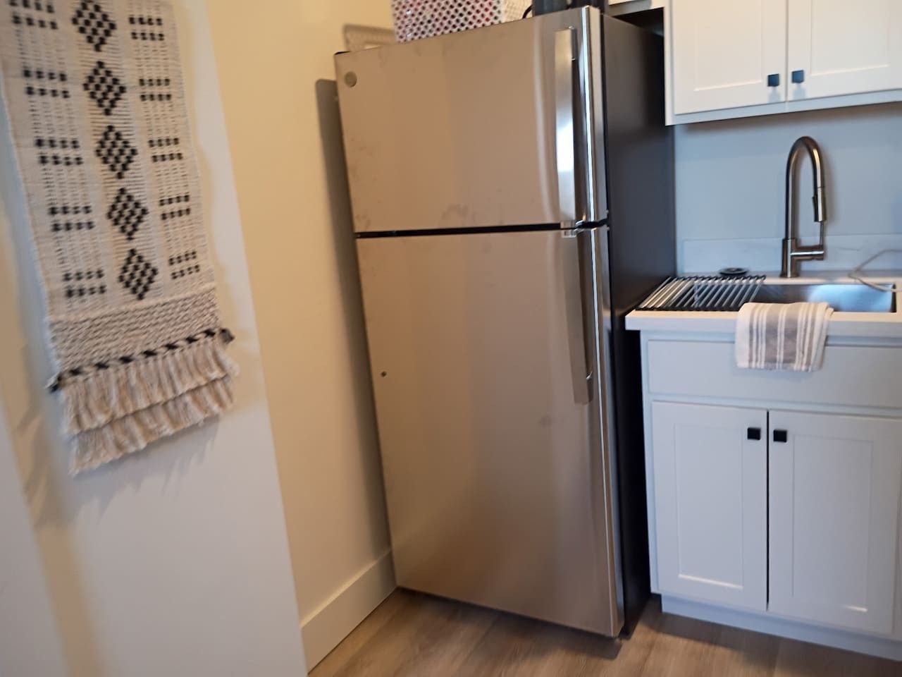 A kitchen with a stainless steel refrigerator, white cabinets, and a sink.