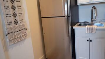 A kitchen with a stainless steel refrigerator, white cabinets, and a sink.