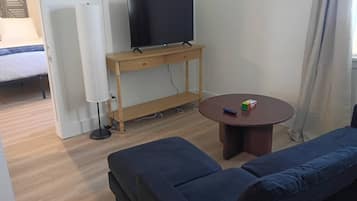 Una sala de estar con un televisor sobre un mueble de madera, una mesa redonda de centro con un Cubo de Rubik, y un sofá azul.