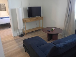 A living room with a television on a wooden stand, a round coffee table with a Rubik's cube, and a blue sofa. - 310 - Historic Charm at The George - New 1BR (Klamath Falls)