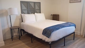 A bedroom with a bed, a side table, a lamp, a radiator, and a wall-mounted sign.