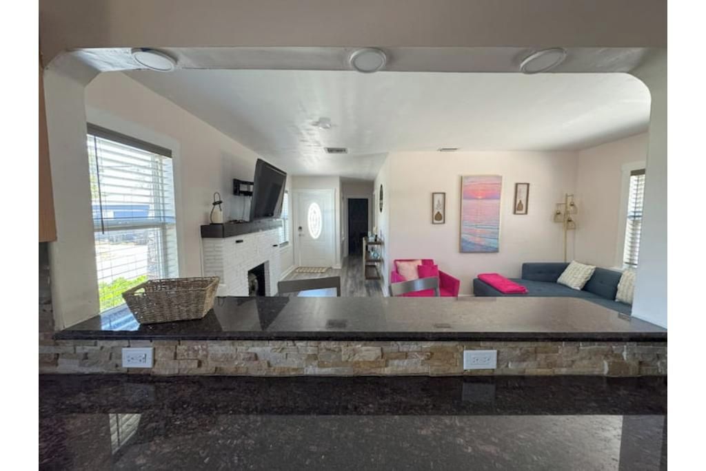 A modern kitchen with a stone countertop, a dining area with a sofa, and a view of the outdoors through large windows.
