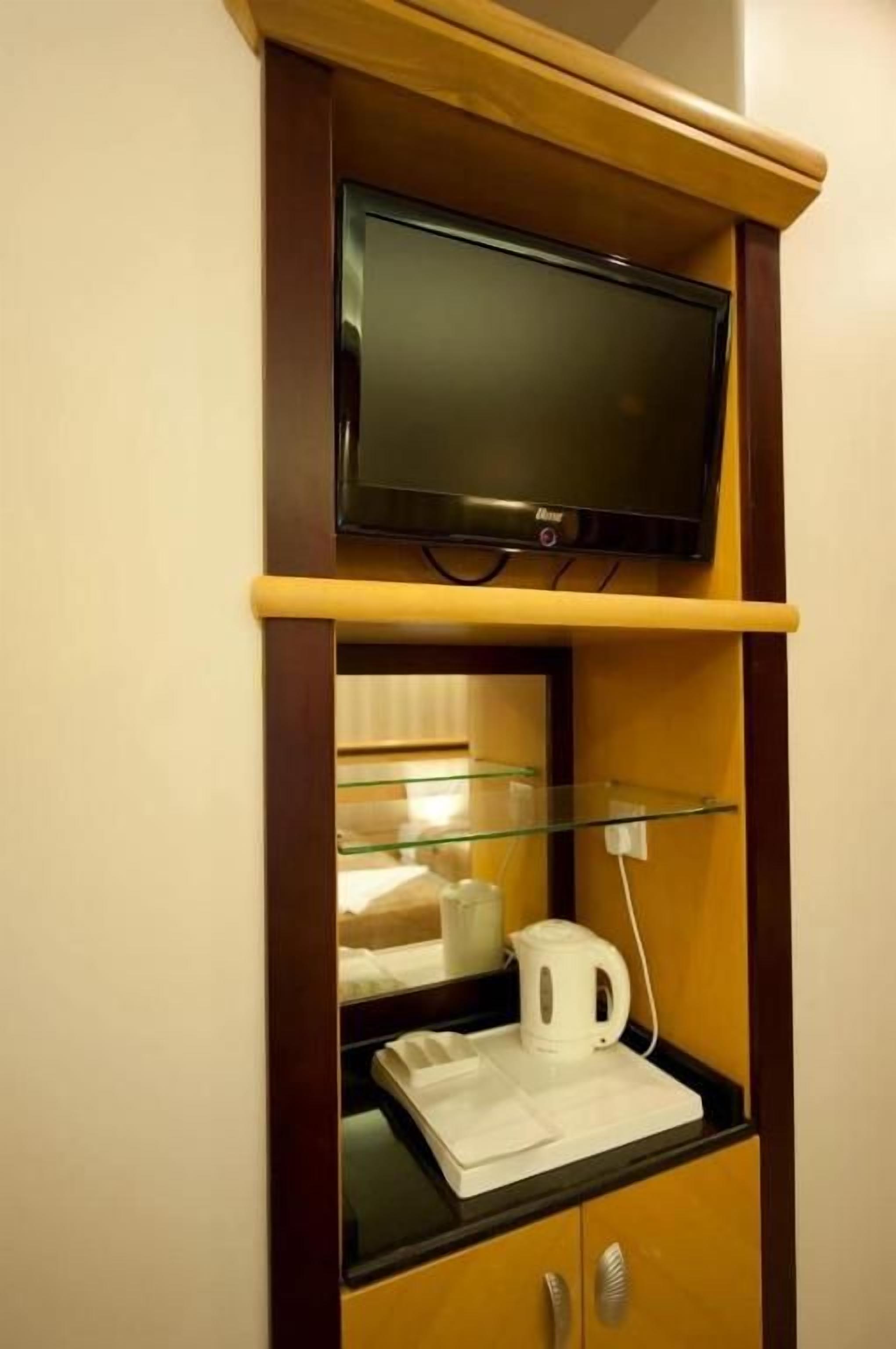 Un televisor montado en un estante de madera sobre una mesa de centro de vidrio, con una tetera blanca y una taza blanca encima.