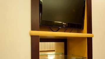 Un televisor montado en un estante de madera sobre una mesa de centro de vidrio, con una tetera blanca y una taza blanca encima.