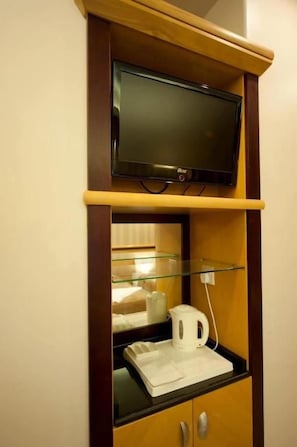Un televisor montado en un estante de madera sobre una mesa de centro de vidrio, con una tetera blanca y una taza blanca encima.