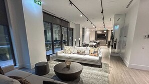 A modern hotel lobby with a sofa, coffee table, and a dining area in the background. - Stylish 1bed 1bath | pool|gym | Central (Toronto)
