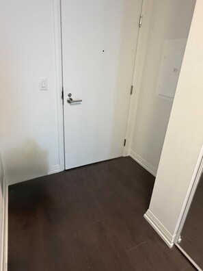 A room with a closed white door, a visible light switch, and a dark brown floor. - Stylish 1bed 1bath | pool|gym | Central (Toronto)