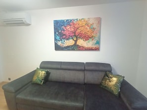 A room with a dark-colored sofa, two decorative pillows, and a colorful abstract painting on the wall. - Apartament Radiostacja VI, trzypokojowe, klimatyzacja, parking free (Gliwice)