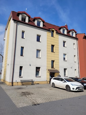 A multi-story building with a red roof, a central entrance, and a car parked in front. - Apartament Radiostacja VI, trzypokojowe, klimatyzacja, parking free (Gliwice)