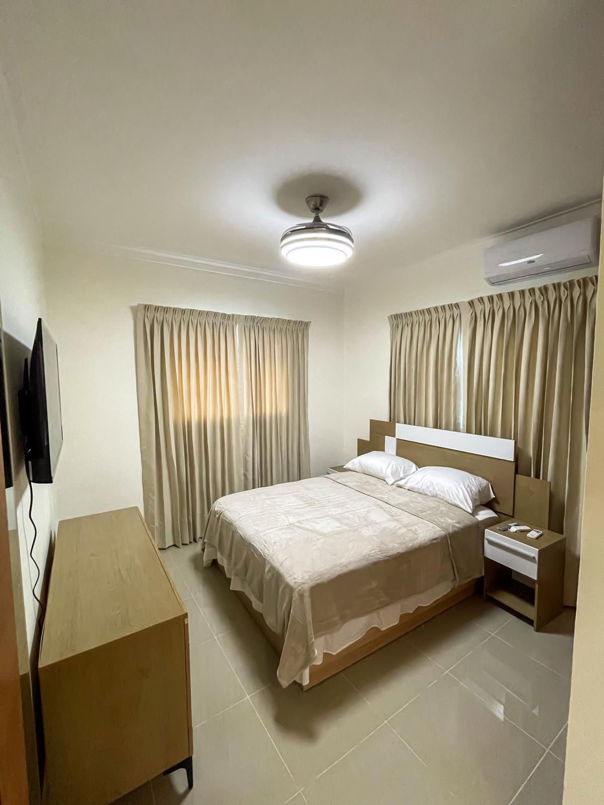 A hotel room with a bed, bedside table, and a television.