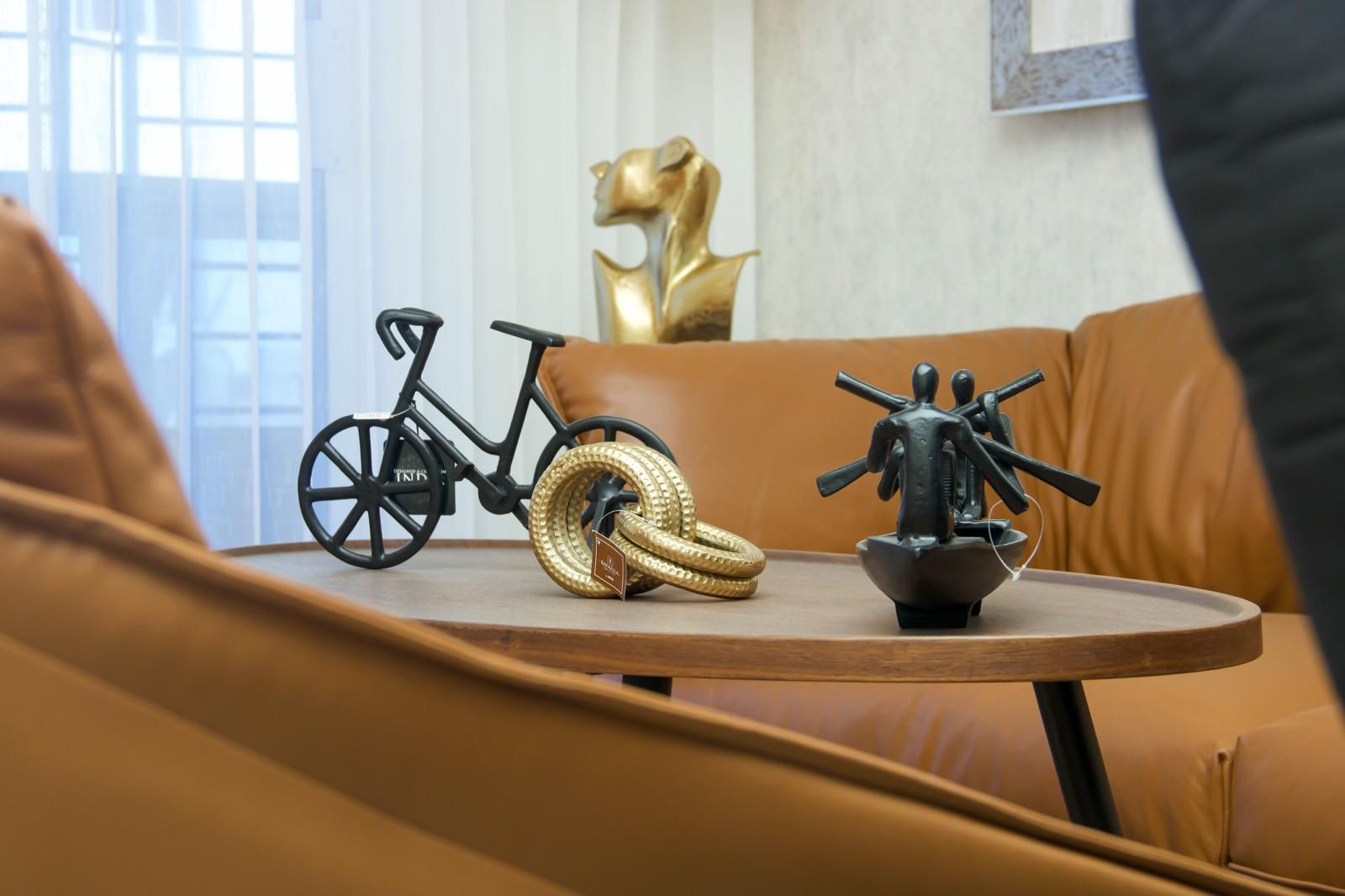 A round wooden table with a bicycle, a golden coiled object, and a black sculpture.