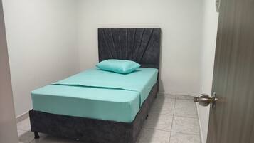 A small, single-bed room with a grey headboard, a teal bedspread, and a single light blue pillow.