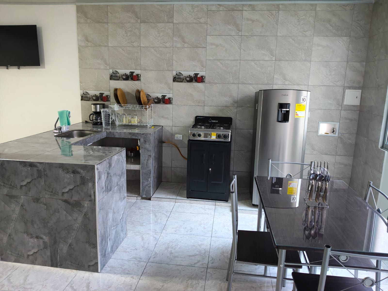 A modern kitchen with a marble countertop, a gas stove, a refrigerator, and a dining area with a glass table and chairs.