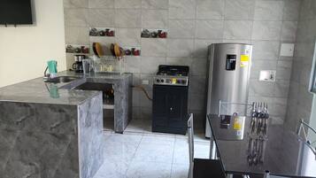 A modern kitchen with a marble countertop, a gas stove, a refrigerator, and a dining area with a glass table and chairs.